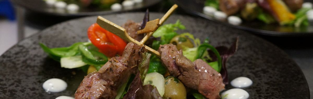 Gegrilde runderpuntjes met gemengde sla, paprika en olijven, mooi opgemaakt op een zwart bord