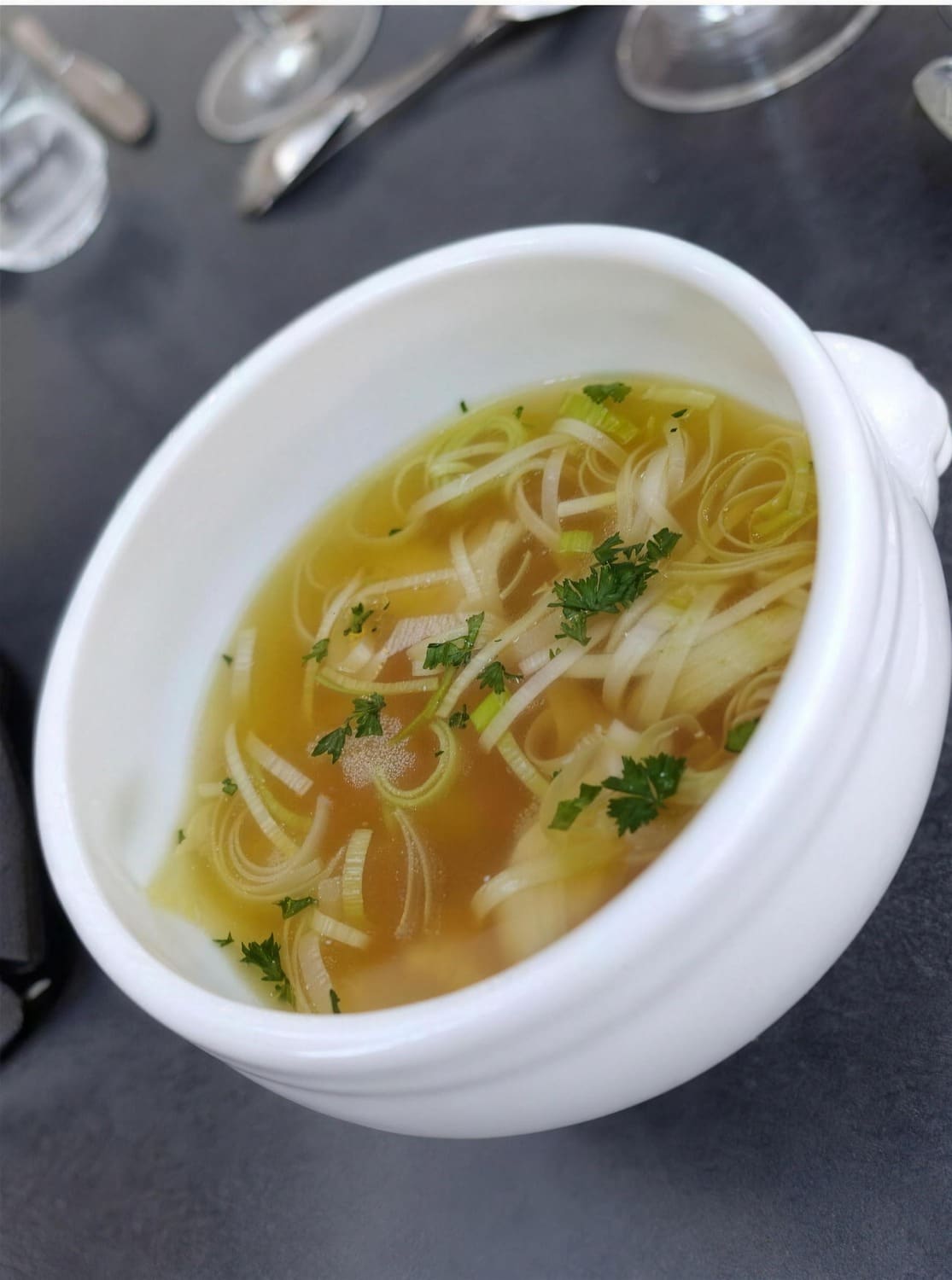 Heldere bouillon met reepjes prei en verse kruiden, uit een eerder maandmenu